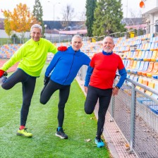 Drie oudere mannen rekken zich uit op de atletiekbaan
