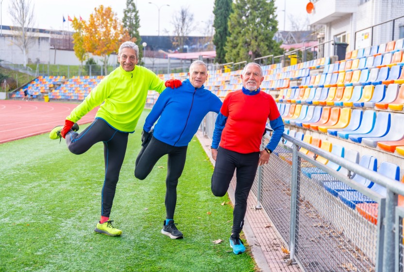 Drie oudere mannen rekken zich uit op de atletiekbaan